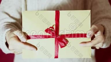 漂亮的女孩拿着一个带有红色丝带的礼物信封。 漂亮的女孩手里拿着一个带有红丝带的礼物信封