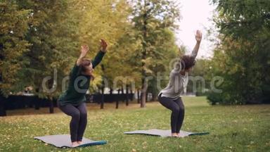 灵活的女孩正在练习椅子姿势，站在公园的瑜伽垫上，移动身体和头部。 美丽的秋天