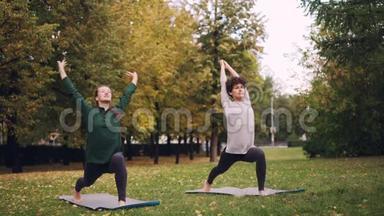 微笑的女孩瑜伽老师和学生在户外的草地上锻炼，在绿色的垫子上练习瑜伽