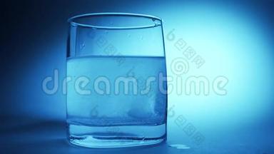 阿司匹林或泡腾药丸在蓝色背景下缓慢滴入一杯水中