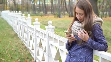 白人妇女戴着针织围巾，使用智能手机，在秋天公园<strong>散步</strong>时打字。 <strong>视频</strong>4k