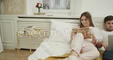 年轻的<strong>女士</strong>和男人在时髦的卧室里放松，躺在床上，<strong>女士</strong>看书，男人看着。