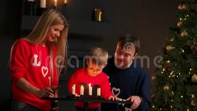 一家人在圣诞节坐在树下看着孩子吹灭蜡烛，笑。 妈妈爸爸笑着