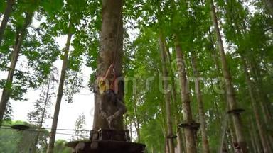 一个小男孩在森林探险公园的树梢上的高空滑索上穿着安全装备的慢速镜头。 室外