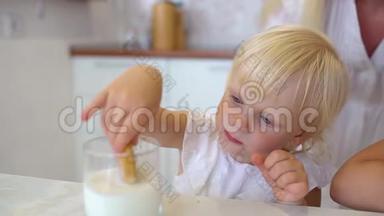 一个金发可爱的小女孩坐在家里的厨房里<strong>吃饼干</strong>的画像