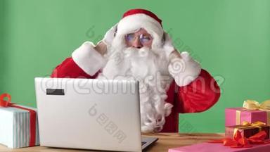 圣诞老人微笑着坐在笔记本电脑后面听着耳机上的音乐和跳<strong>舞</strong>，<strong>背景</strong>是绿色的色度