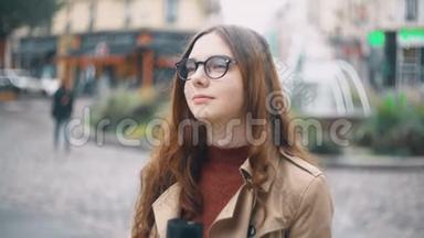 年轻漂亮的法国学生戴着眼镜站在街上，喝着帽子上的茶，对着镜头微笑的肖像。