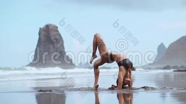 一位身穿<strong>泳装</strong>的美女在<strong>海滩</strong>上表演一座运动桥，桥上环绕着黑色的火山沙