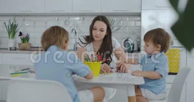 两个男孩的孩子和他的母亲坐在厨房里画画。 家庭幸福。 兄弟们在桌子旁画画。 实际