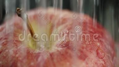 在视频中，我们看到一个红苹果，水开始从顶部倾泻，就像淋浴，黑色背景，特写。