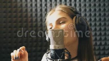 在录音室唱歌的漂亮女孩的肖像。 年轻歌手有感情地录制新歌。 女士唱歌