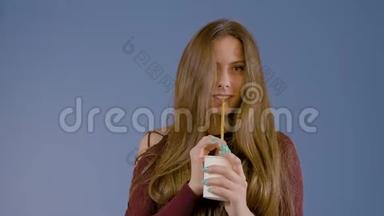 一个年轻的女孩拿着一个纸杯喝酒。 在蓝底的工作室里。 <strong>广告摄影</strong>。