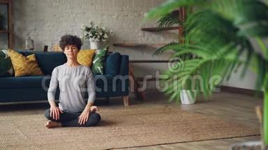 放松的年轻女士正<strong>坐在</strong>公寓<strong>地板上</strong>的火木中，摆出一副agnistambhasana的姿势，在瑜伽的过程中呼吸进出