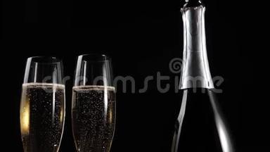 好香槟酒。 两个带香槟的玻璃杯和一个带香槟的瓶子，放在黑色背景的木桌上。 长笛