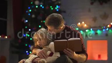 <strong>专心</strong>致志的爸爸在装饰好的树旁为困倦的女孩读圣诞童话