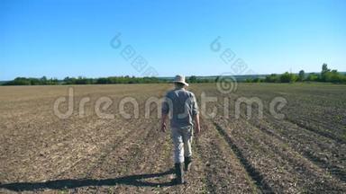 在阳光明媚的<strong>夏日</strong>里，戴着<strong>帽子</strong>和衬衫的年轻男农场主在他的田野上穿过绿色的小芽