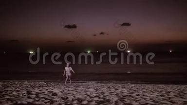 在日落时沿着海滩散步的快乐女孩的剪影。 动作缓慢。 孩子在海滩上奔跑，抚养