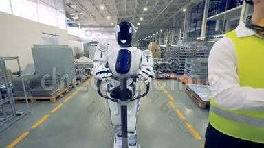 一个类似人类的机器人正在和一个工厂工人一起行走时拉着一个工厂的运输工
