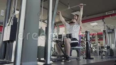 男人在健身房的训练模拟器上与私人教练摆动手臂肌肉。 个人减肥训练