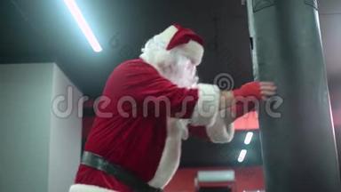 圣克劳斯拳击手与红色绷带拳击手击打一个巨大的拳击袋在拳击工作室。 圣诞老人拳击手