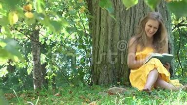 可爱的女孩子穿着黄色的衣服<strong>坐在</strong>老<strong>树下</strong>，在夏天的公园里读小说。 4K