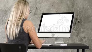 女商人坐在办公室的办公桌前，用桌面显示器工作。 白色显示器。