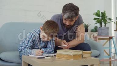 勤奋的小学生在<strong>作业本</strong>上写作业，而他慈爱的父亲在帮助他。 教育