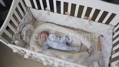 两个月大的男孩穿着蓝色婴儿滑块躺在家里的卧室婴儿床上。 小男孩想在床上睡着
