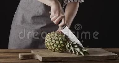 女厨师`她的手正在把新鲜的天然菠萝切成两半，放在厨房的木板上，放在黑色的桌子上