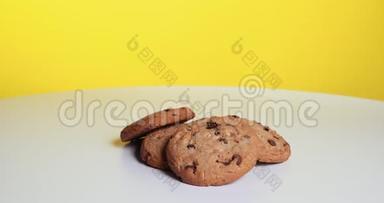 带有巧克力片和葡萄干的美式饼干在黄色背景的白色桌子上旋转。 职业介绍所