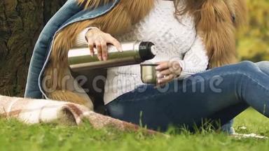 女孩用<strong>热水</strong>瓶<strong>倒</strong>茶，在秋天的森林里享受热饮