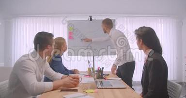 四个大联盟在办公室室内开会的肖像。 商人在白板上画一张图表