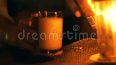 夏季夜晚海滩酒廊，用蜡烛将一杯泡沫汽水倒入桌上的玻璃杯中，拍摄特写镜头