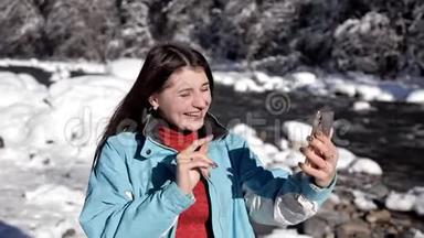 冬天森林里靠近山河的女孩用手机在视频上聊天