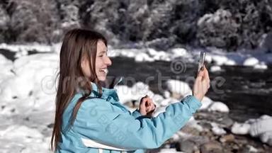 冬天森林里靠近<strong>山河</strong>的女孩用手机在<strong>视频</strong>上聊天