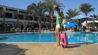 酒店游泳池附近带粉红色箱子的年轻女子。 旅行度假概念