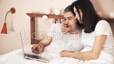 快乐的一对情侣在床上用笔记本电脑在网上购物