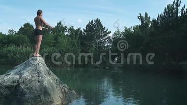 暑假或度假的年轻人从山林湖中央的石头上跳下来。 跳跃到