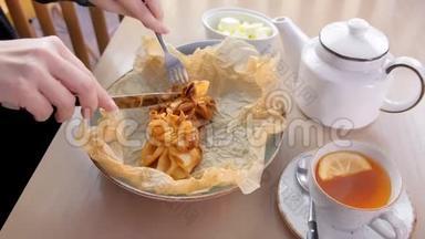 女人正在吃朱莉安烘焙的面团，放在面包纸上，上面有茶和黄油。 双手特写..