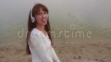 年轻女孩带着耳机在沙滩上散步，一边用平板电脑听音乐，一边笑着跳舞