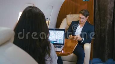成功的商人驾驶私人飞机。 在笔记本电脑上工作。 使用智能手机。 商人和女商人