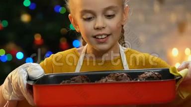 小女孩拿着蛋糕放在烤盘里，为自己做糖果而自豪
