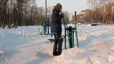 穿着带罩的蓝<strong>羽绒服</strong>的人在一个冬季城市公园里从事滑雪模拟器。 后景。