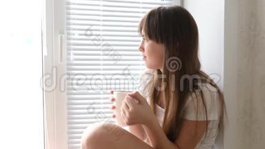 小女孩早上在<strong>窗边</strong>喝茶。 美丽的女孩看着<strong>窗</strong>外，手里拿着一杯茶。