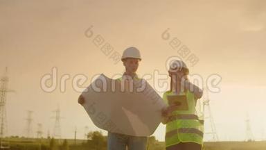 两名电工一起工作，戴着头盔站在输电线路附近的田野里。站在