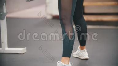 一个正在健身房训练腿脚的女人，手里拿着一个铁哑铃，身体向下倾