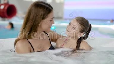 一位美丽的年轻母亲和可爱的女儿在热水浴缸里的肖像。