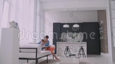 一位年轻的母亲带着一个孩子读一本书，坐在客厅里明亮的白色屋子里