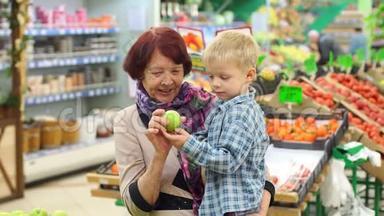 一位老年妇女带着她的小孙子在大型超市买新鲜苹果。