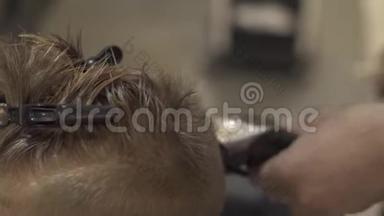 儿童发型师在美发沙龙用电动剃须刀切割小男孩。 海丽丝师做儿童发型